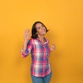 Welcoming woman waves smiling coquettishly at camera. Cute young brunette wearing jeans and checkered shirt showing Royalty Free Stock Photo