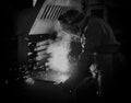 Welder at the factory in a welding mask welds metal parts, welding and sparks, black and white, manufacturing