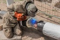 A welder in a protective shield is engaged in welding work on the polyethylene pipe of the heating main pipeline at the