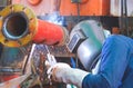 Welder with safety equipment is welding steel pipe in outdoors workshop for use in oil pipeline system renovate work