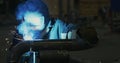 Welder in welding mask, in working clothes at the factory, welds the pipe in the factory room.