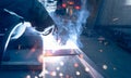 Welder welding metal with argon arc welding machine and has welding sparks and smoke. Man wear protective gloves. Safety in