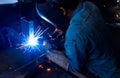 Welder welding metal with argon arc welding machine and has welding sparks. A man wears welding mask and protective gloves. Safety