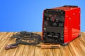 Welding machine with stick electrode holder, work cable and clamp on the wooden table. 3D rendering