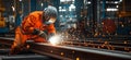 Welding worker in orange jumpsuit creating sparks in industrial workshop environment Royalty Free Stock Photo