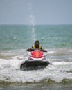 Handsome Jetsky rider wearing sunglasses and a yellow jacket moves towards the beach, front view