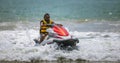 Handsome Jetsky rider wearing sunglasses and a yellow jacket riding a jet ski on the beach