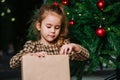 Well behaved girl sitting under a christmas tree, looking at wrapped present