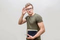 Well-build and strong young man posing on camera. He looks straight and hold hand on glasses. Guy has books in other