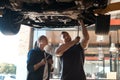 Well do a better job in half the time. two mechanics working together under a lifted car. Royalty Free Stock Photo