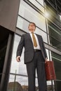 Well dressed businessman with briefcase standing talking on the phone in front of modern glass building  with sun reflection. Pers Royalty Free Stock Photo