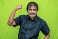 A man in a black shirt stands against a green screen, appearing to celebrate a win as he raises his right hand in a closed fist