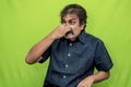 A disgusted businessman in black shirt holds his nose with right hand while standing against a green screen due to the foul smell