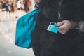 Well-dressed lady in fur holding credit card and bag at blurred mall background. Woman paying in fashion boutique giving bank card