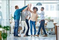 Well get it done together. a positive group of coworkers high-fiving each other while standing in the office.