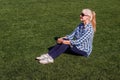 Well-groomed Caucasian woman fifty years in a plaid shirt and jeans sitting on the grass