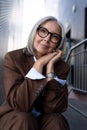 well-groomed healthy slender gray-haired mature business lady dressed in a stylish brown jacket sits against the