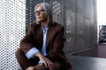 well-groomed healthy slender gray-haired mature business lady dressed in a stylish brown jacket sits against the