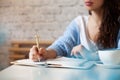 Well groomed woman hand holding gold pen and writing notes with gold pen in notebook. cup of hot butterfly pea latte or Royalty Free Stock Photo