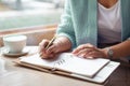 Well groomed woman hand holding gold pen and writing notes with gold pen in notebook beside window. Royalty Free Stock Photo