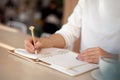 Well groomed woman hand holding gold pen and writing notes with gold pen in notebook beside window. Royalty Free Stock Photo