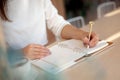 Well groomed woman hand holding gold pen and writing notes with gold pen in notebook beside window. Royalty Free Stock Photo