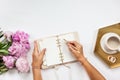 Well-groomed woman hands is writing in diary with stationery supplies set onside and peonies bouquet Royalty Free Stock Photo