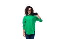 well-groomed young female marketing employee with black hair dressed in a green shirt showing a screen of a mobile phone