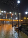 Well-lit city park at night with ornate street lamps and benches on a wet, brick-paved walkway. Calm and modern urban