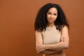 Well-looking lady with brunette curly hair looking at camera and smiles, holding arms crossed. Waist up portrait view of