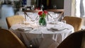 Well-set round table covered with white tablecloth in restaurant. Each place including plate, nappkin and two glasses