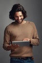 Well thats good to know. Studio shot of a handsome young man using a digital tablet against a gray background.