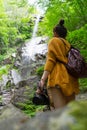 Wellbeing photographer enjoying splash of hidden waterfall. Fit lady hold camera on hand traveling alone with backpack on