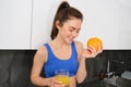 Wellbeing and sport. Young smiling nutritionist, fitness girl holding orange and fresh juice, drinking it from glass and Royalty Free Stock Photo