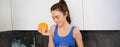 Wellbeing and sport. Young smiling nutritionist, fitness girl holding orange and fresh juice, drinking it from glass and Royalty Free Stock Photo