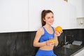 Wellbeing and sport. Young smiling nutritionist, fitness girl holding orange and fresh juice, drinking it from glass and Royalty Free Stock Photo