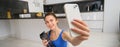 Wellbeing and sports. Beautiful young woman taking selfie on smartphone, doing fitness training from home, drink water Royalty Free Stock Photo