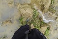 Wellies from the first person perspective, gazing at the muddy ground. A watercourse flows from a puddle. Carmouflage in