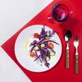 Wellness food - fresh salad of tomato, cucumber, red cabbage on white plate in hard light with shadow with drink on red background