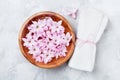 Wellness and spa composition of perfumed pink flowers water in wooden bowl and terry towel on gray stone table. Aromatherapy. Royalty Free Stock Photo