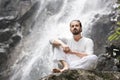 Wellness yoga meditation concept. Young man sitting in lotus position on the rock under tropical waterfall. Royalty Free Stock Photo