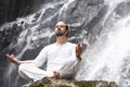 Wellness yoga meditation concept. Young man sitting in lotus position on the rock under tropical waterfall. Royalty Free Stock Photo