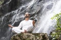 Wellness yoga meditation concept. Young man sitting in lotus position on the rock under tropical waterfall. Royalty Free Stock Photo