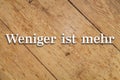 `Weniger ist mehr` text on a wooden background. Translation: `Less is more`