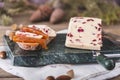 Wensleydale cheese with cranberries, red wine, honey, nuts, raisins on wooden cutting board. Black concrete background Royalty Free Stock Photo