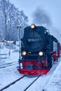 The historic steam locomotive of the Harz narrow-gauge railway enters on the snow-covered tracks at the station in front of the Royalty Free Stock Photo