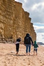 08-29-2020 West Bay, UK. People walking on golden beach underneath towering cliffs on sunny summer day.