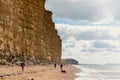 08-29-2020 West Bay, UK. People walking on golden beach underneath towering cliffs on sunny summer day.