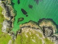 West coast of Ireland. Aerial drone top down view. Green fields and rocky shore. Rocks under water make foot print shape or exclam