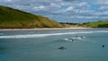 Surfers ride the waves in Clonakilty on a fine summer day. Water sports in Ireland, landscape.